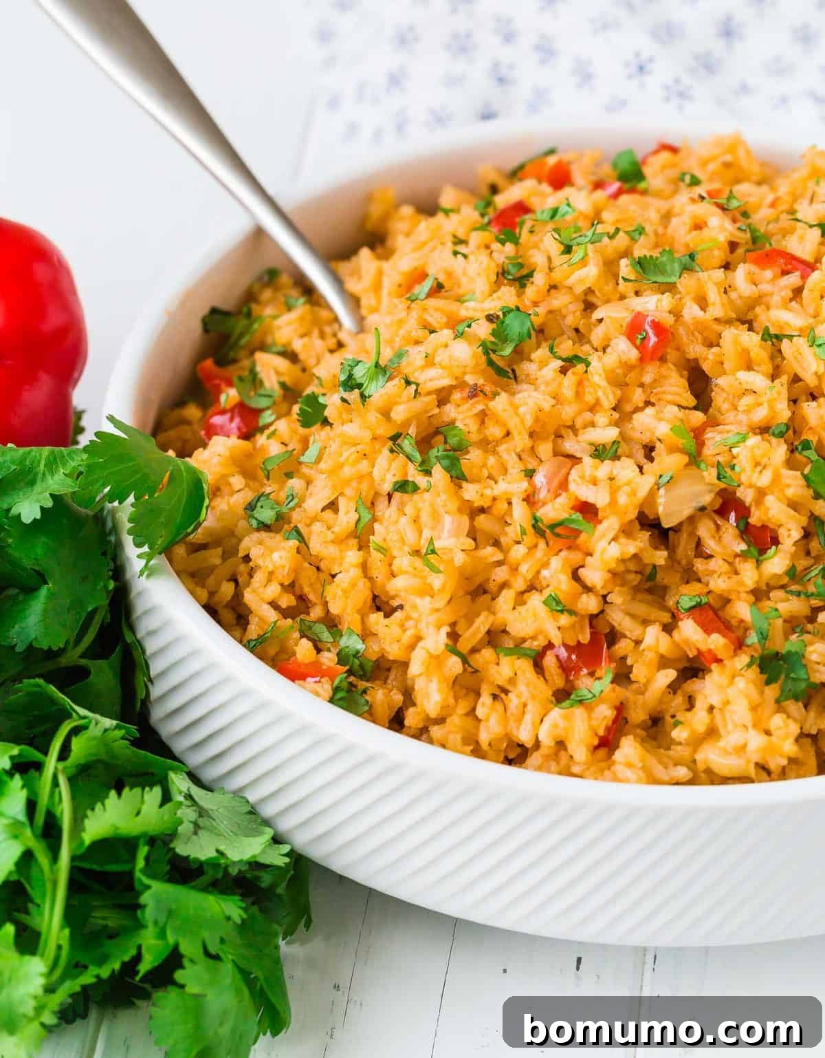 Mexican rice in a white bowl with a silver serving spoon.