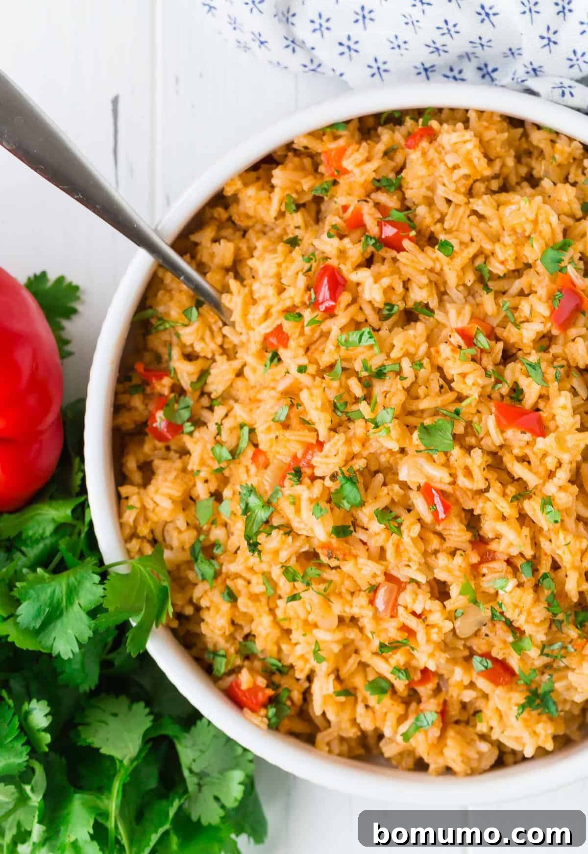 Overhead view of red colored rice in a white serving bowl. Fresh cilantro also visible.