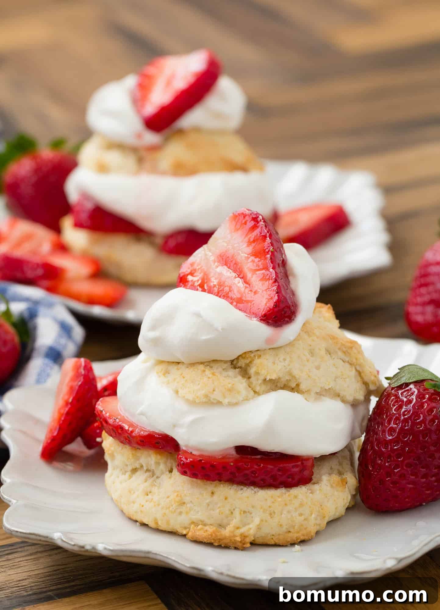 Decorative white plate with strawberry shortcake on it, topped with whipped cream and strawberries.