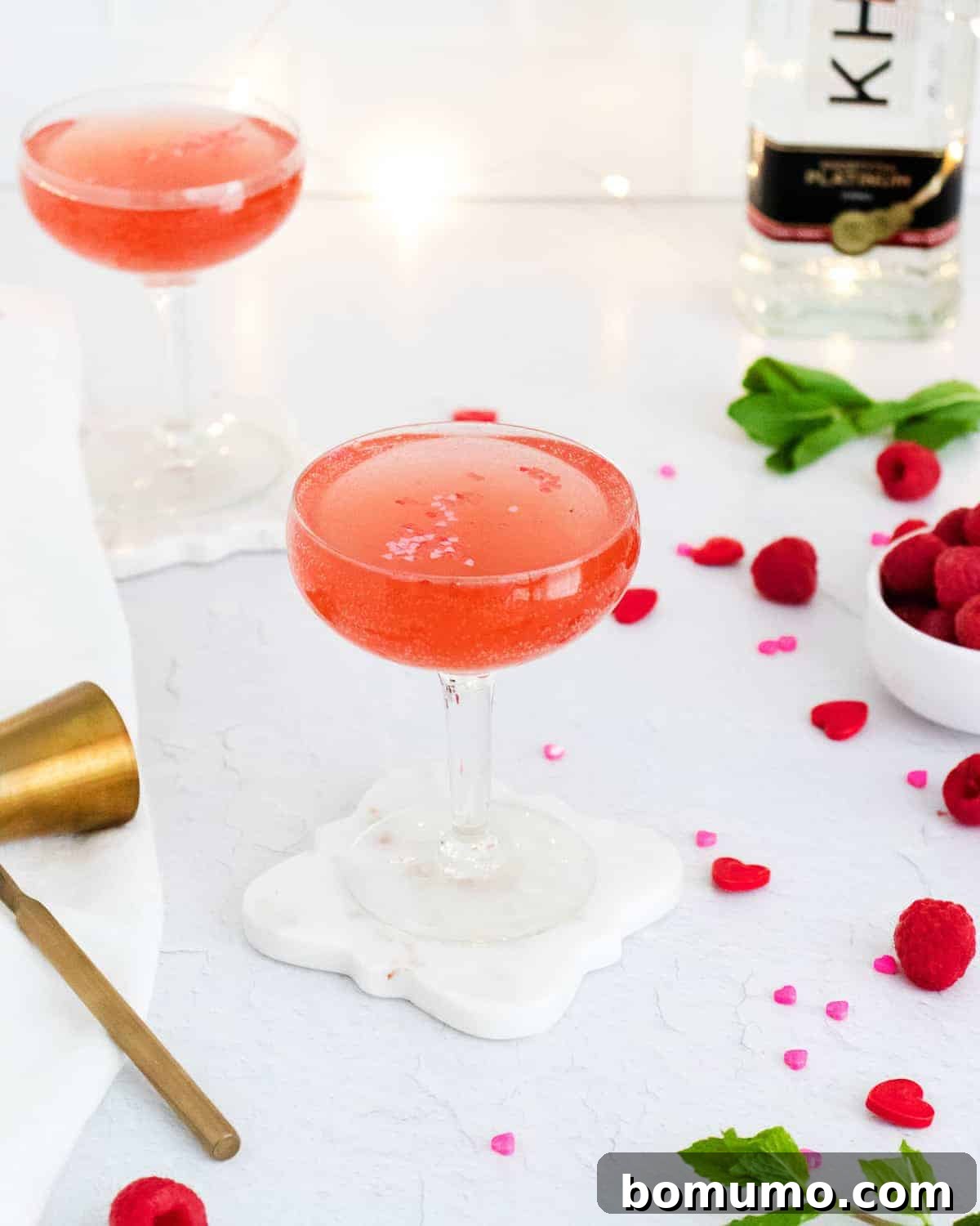 Two pink drinks, with raspberries and fresh mint scattered around, creating a vibrant visual.
