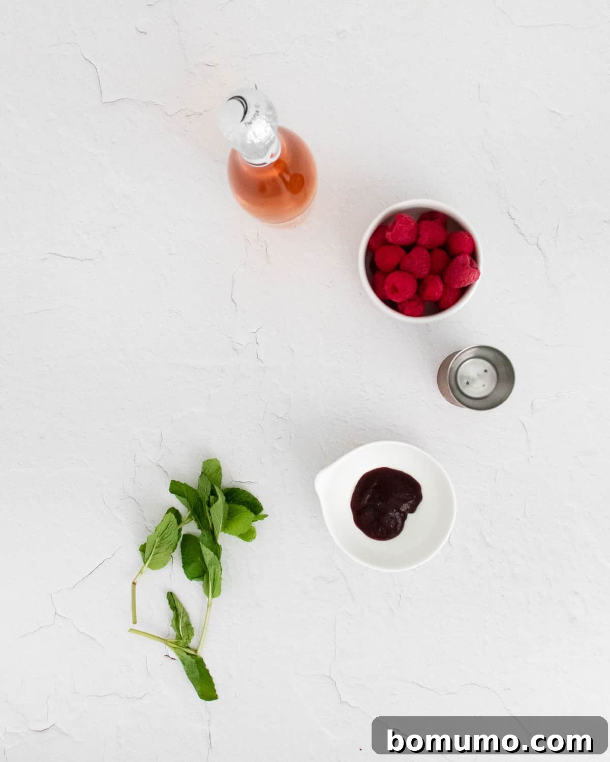 Overhead view of mint, jam, vodka, raspberries, and rosé, showcasing the fresh ingredients.