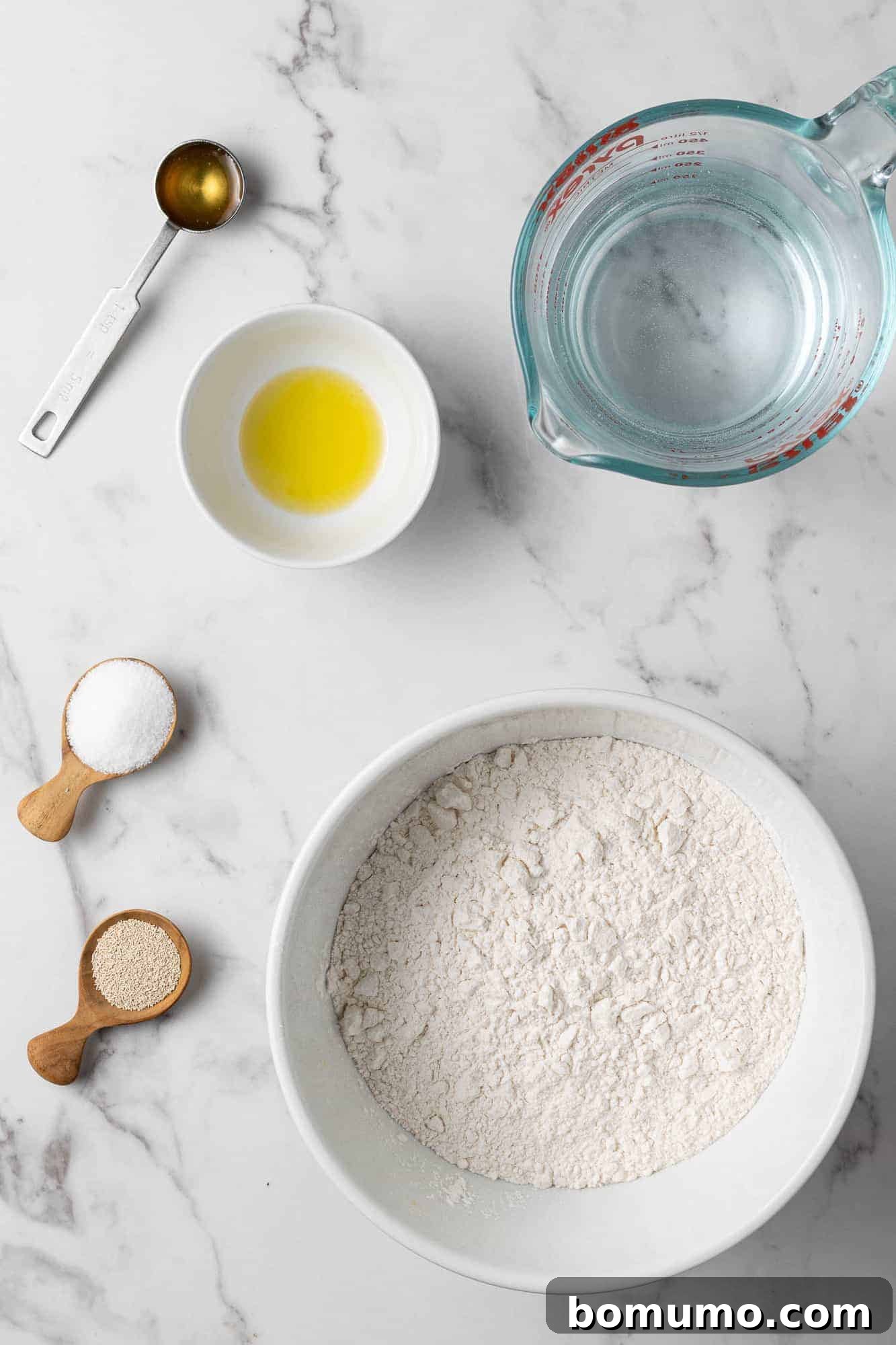 Overhead view of all the simple ingredients laid out for Dutch oven bread: flour, olive oil, instant yeast, water, salt, and honey.