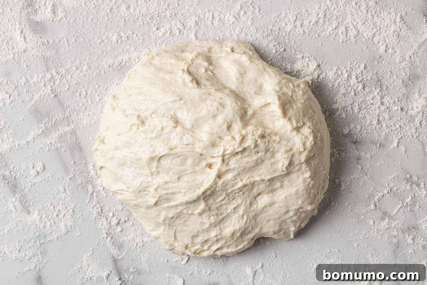 A ball of rustic bread dough resting on a floured surface, ready for its hot Dutch oven bake.