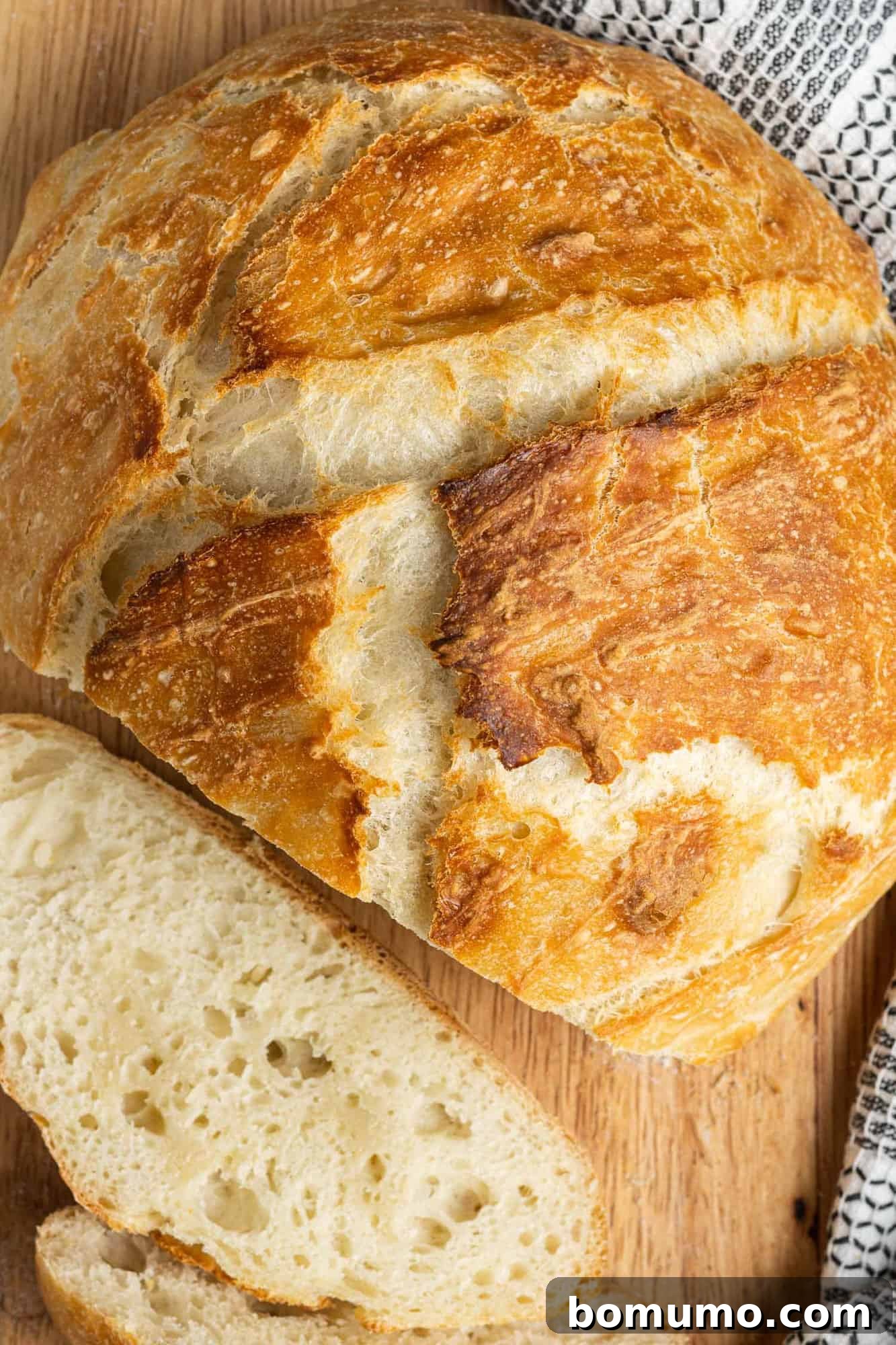 Overhead view of a beautiful round loaf of Dutch oven bread with a few slices already cut, revealing its soft, airy interior.