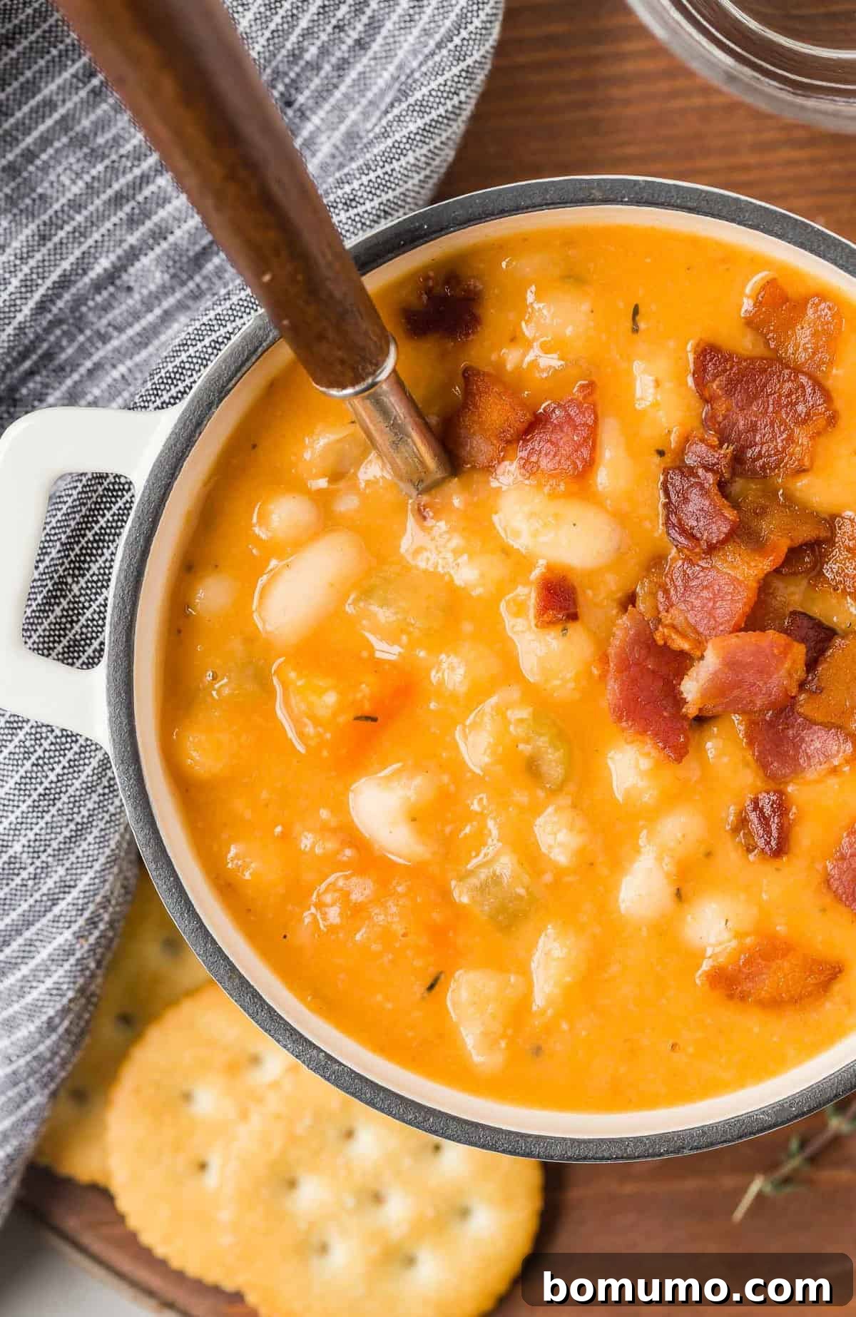 Versatile Bean and Bacon Soup 2 Hearty homemade bean and bacon soup, garnished with crispy bacon bits and a fresh thyme sprig, served alongside golden Ritz crackers for a perfect comfort meal.