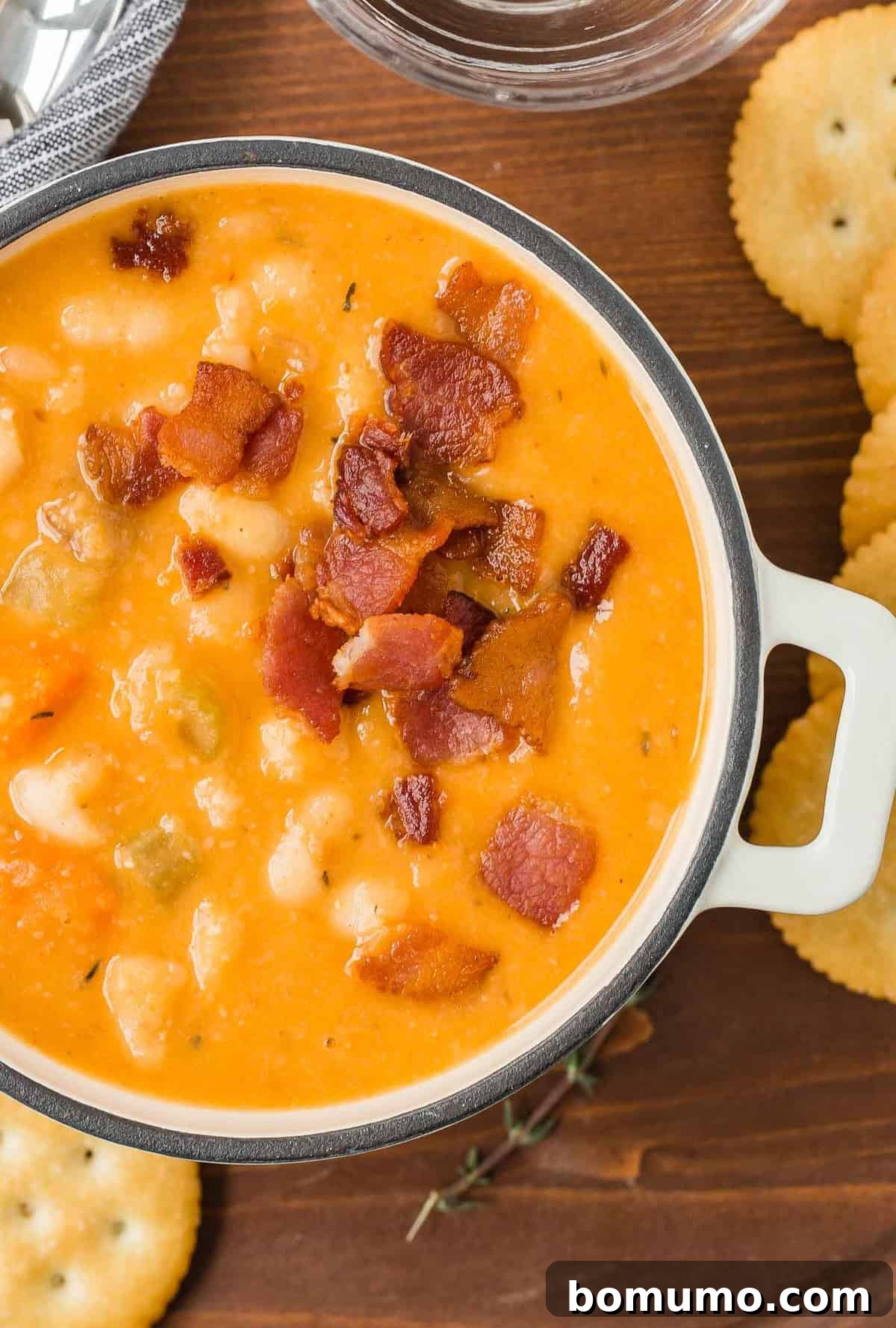 Versatile Bean and Bacon Soup 3 Close-up view of a steaming bowl of homemade bean and bacon soup, perfectly creamy and garnished with fresh herbs, served on a rustic wooden tray with crunchy Ritz crackers.