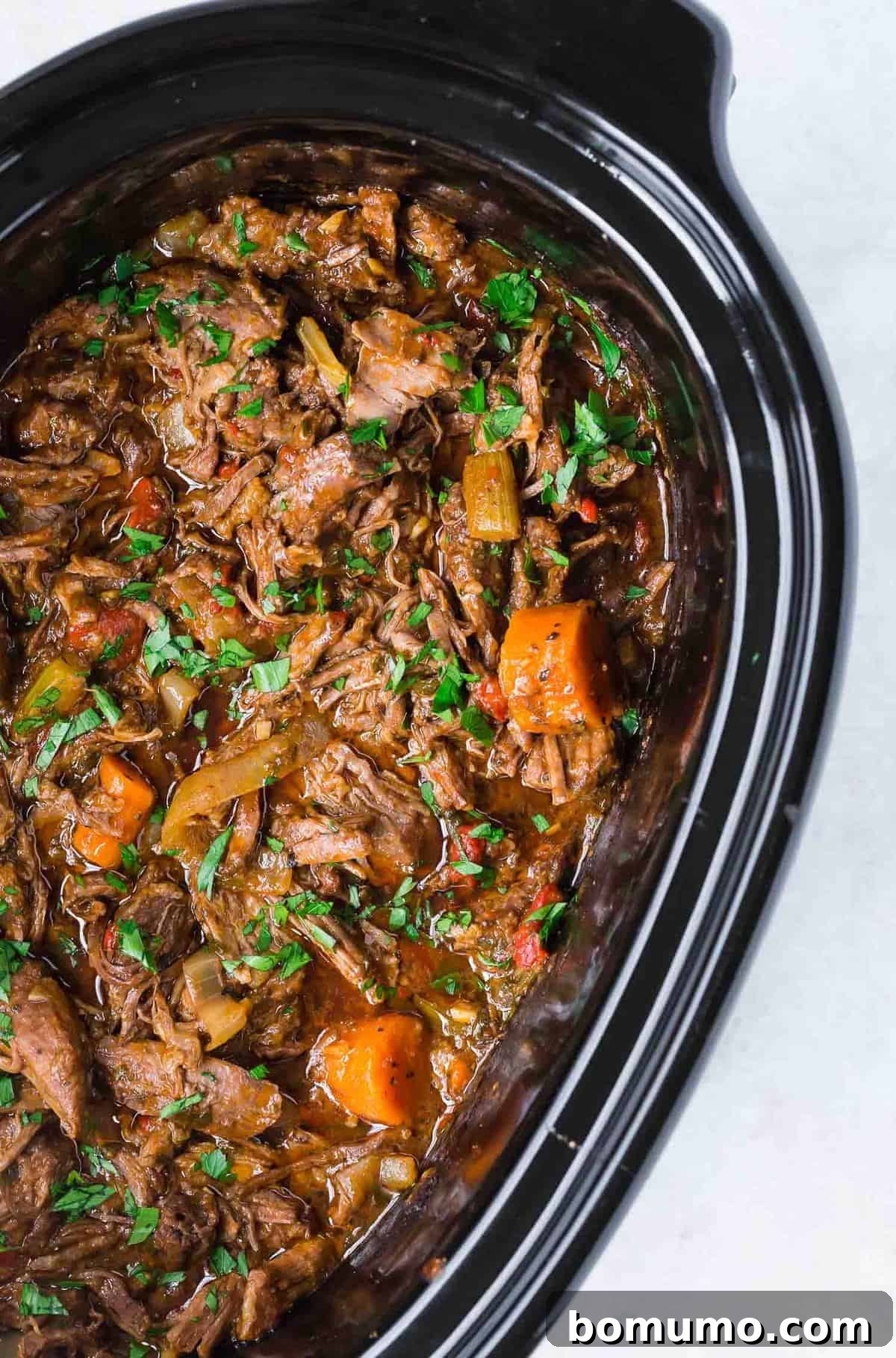 Pot roast and carrots simmering in a black slow cooker, ready to be served.