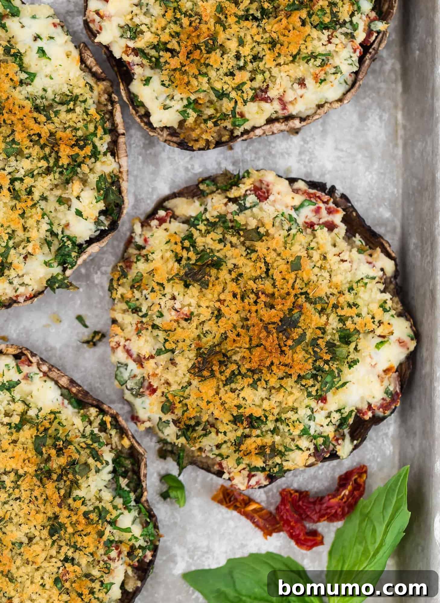 Stuffed Portobello Delight 2 Overhead view of stuffed mushrooms on a baking sheet, garnished with sun dried tomatoes and fresh basil.