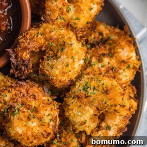 Pile of coconut shrimp on a plate with dipping sauce.