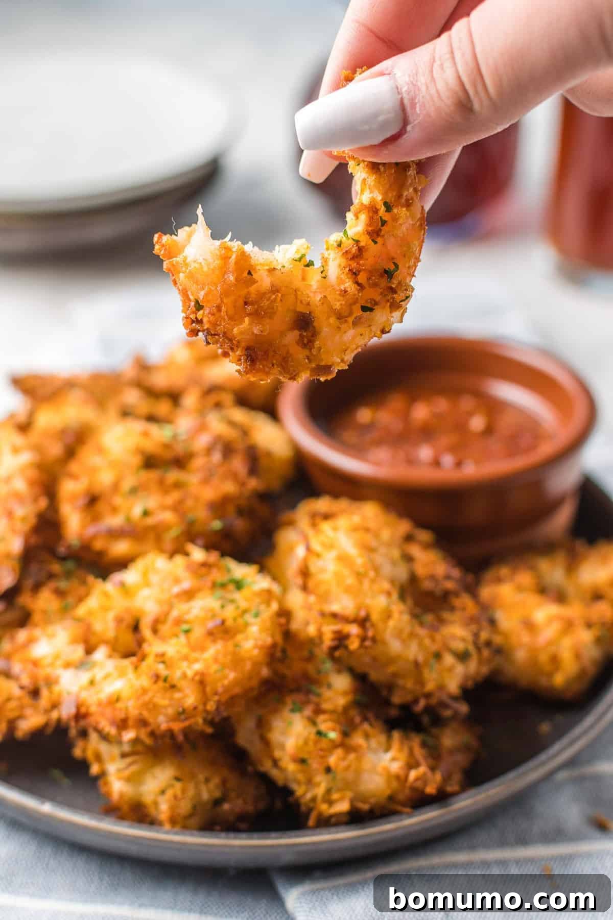 A close-up shot of a crispy air fryer coconut shrimp with a bite taken out of it, revealing the tender shrimp inside and the golden, textured coating.