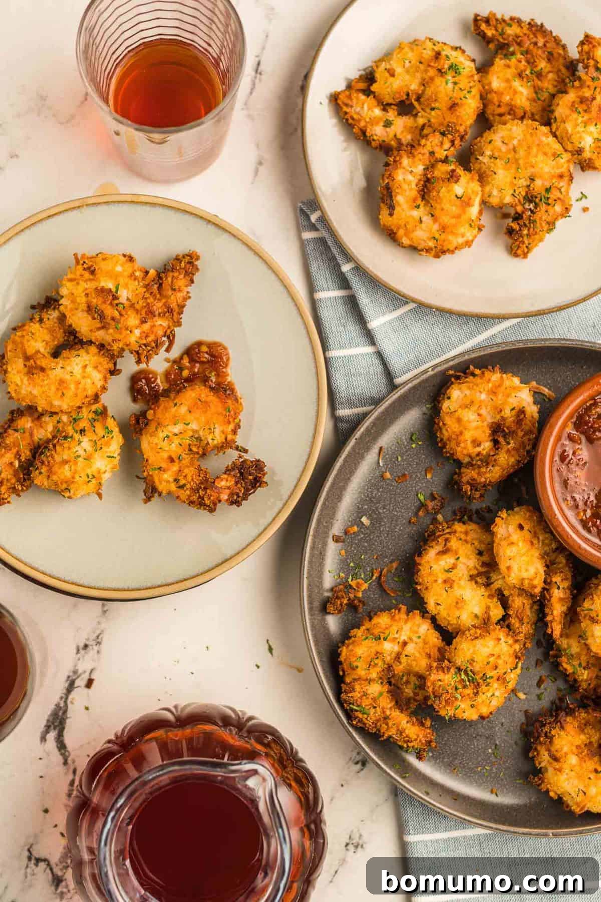 An overhead view of three individual plates, each holding a neat pile of golden brown, crispy air fryer coconut shrimp, suggesting a serving presentation.