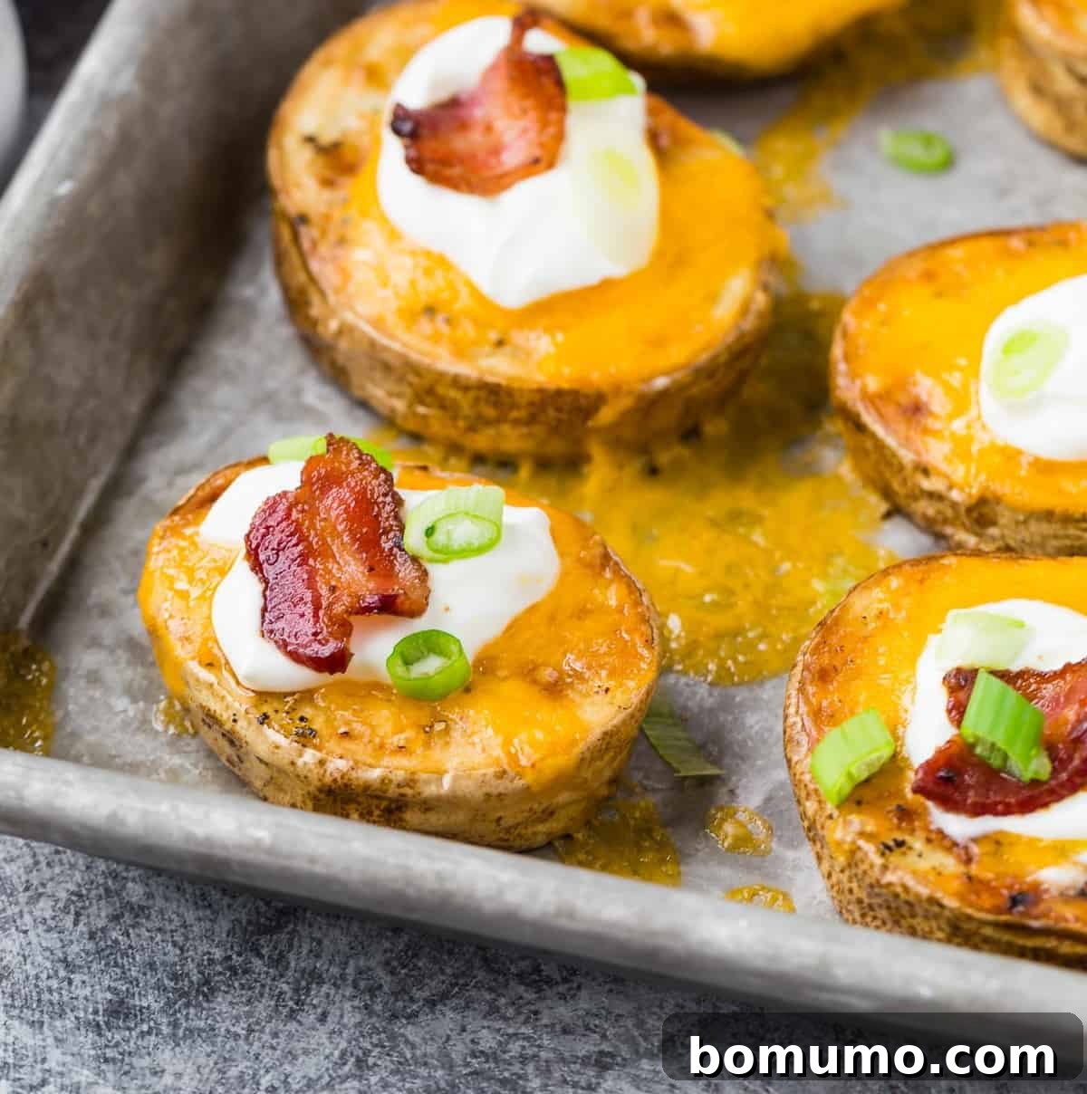 Sliced potatoes on a roasting pan, topped with cheese and toppings.