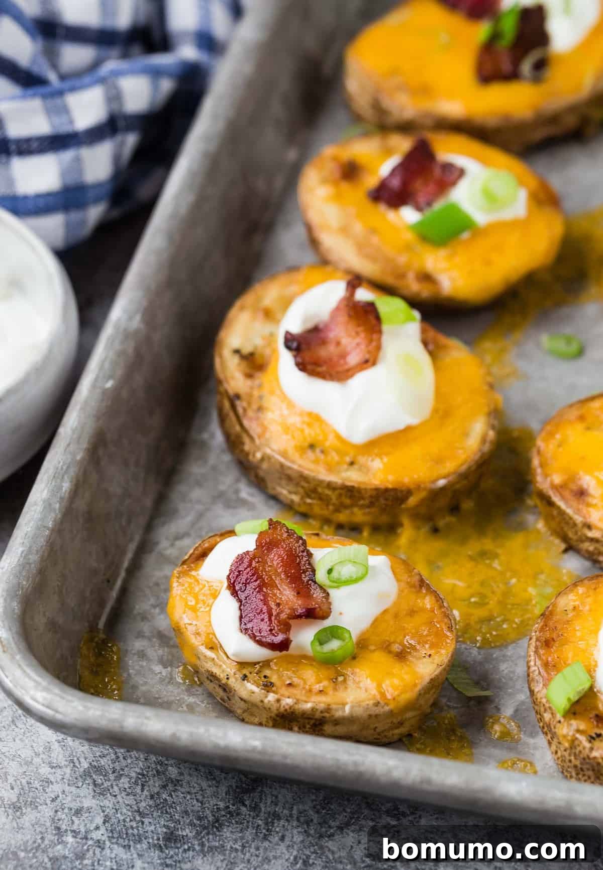Potato rounds on a pan, topped with cheese, sour cream, bacon, green onion.