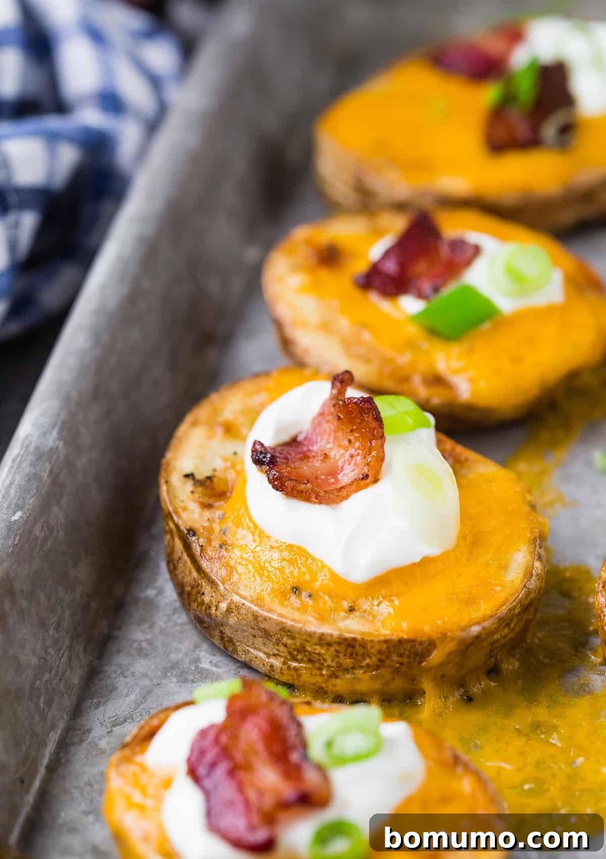 Sliced potatoes with cheese and toppings on a baking sheet. 