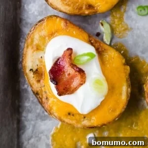 Overhead view of a slice of cooked potato topped with cheddar cheese, sour cream, bacon, and green onion.