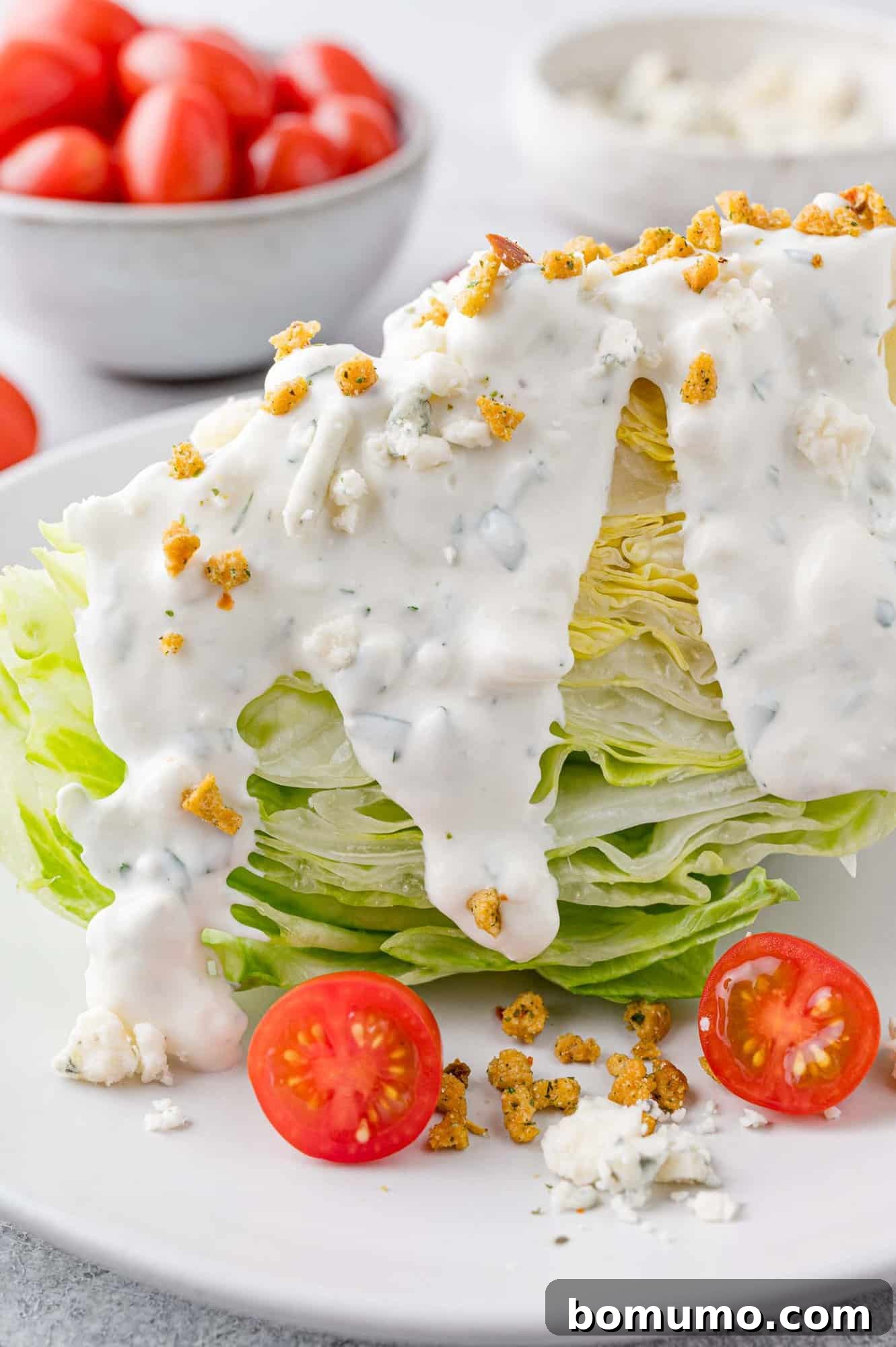 A vibrant wedge salad generously topped with creamy blue cheese dressing, crispy crouton crumbles, and fresh diced tomatoes.