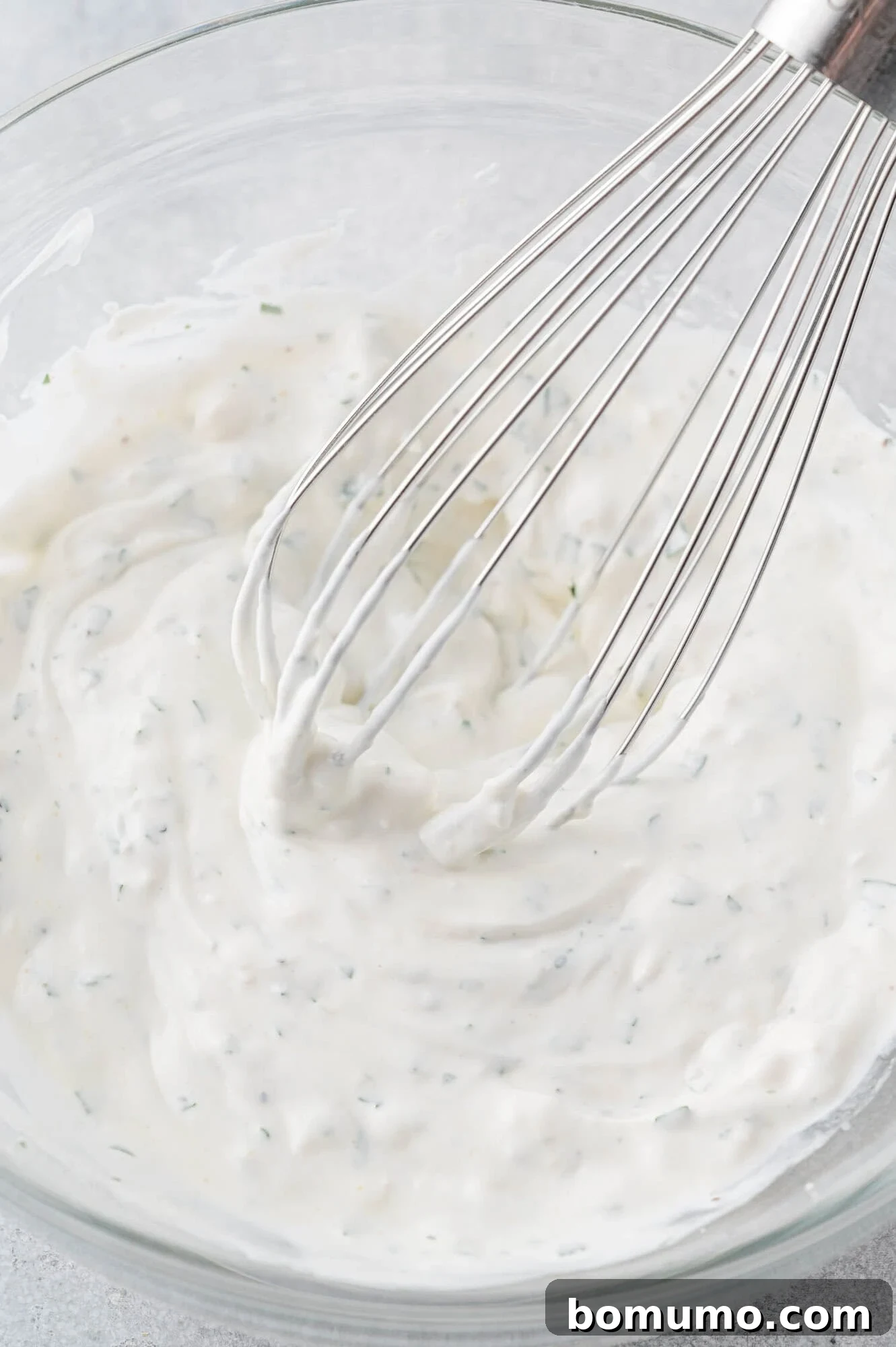 A whisk actively mixing the blue cheese dressing ingredients in a bowl, creating a smooth, creamy texture.