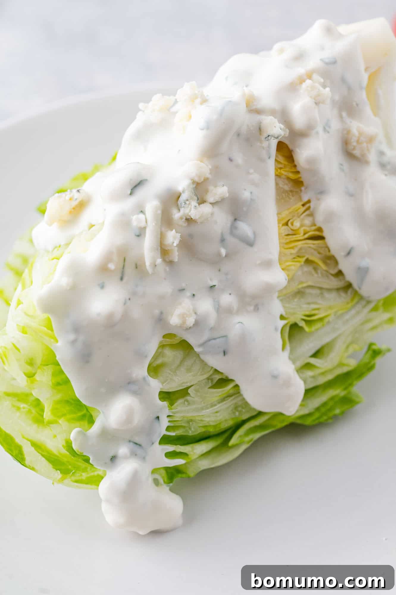 A perfectly spooned serving of blue cheese dressing resting on a crisp wedge of iceberg lettuce, ready to be enjoyed.