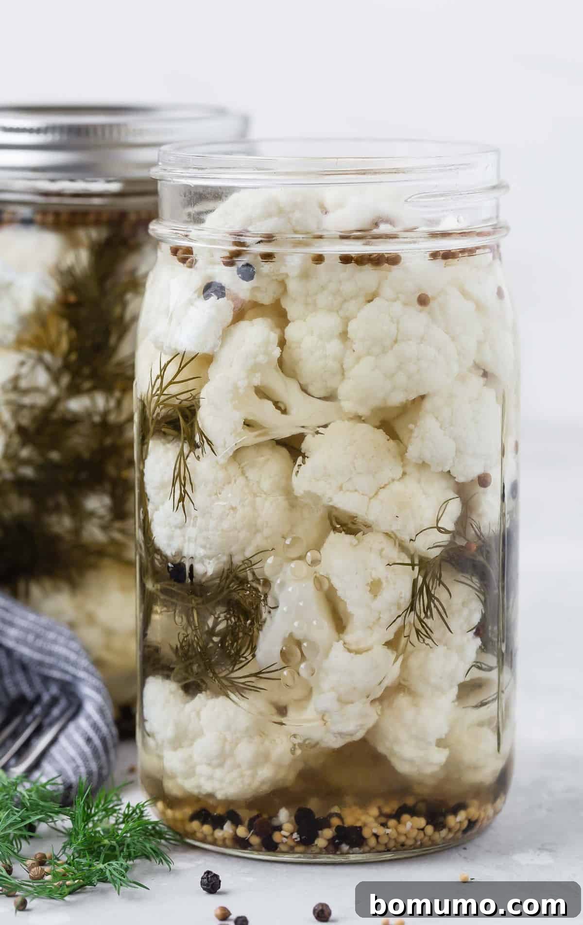 Quick Tangy Cauliflower Pickles 2 Jar of pickled cauliflower with dill and peppercorns, another jar in background.