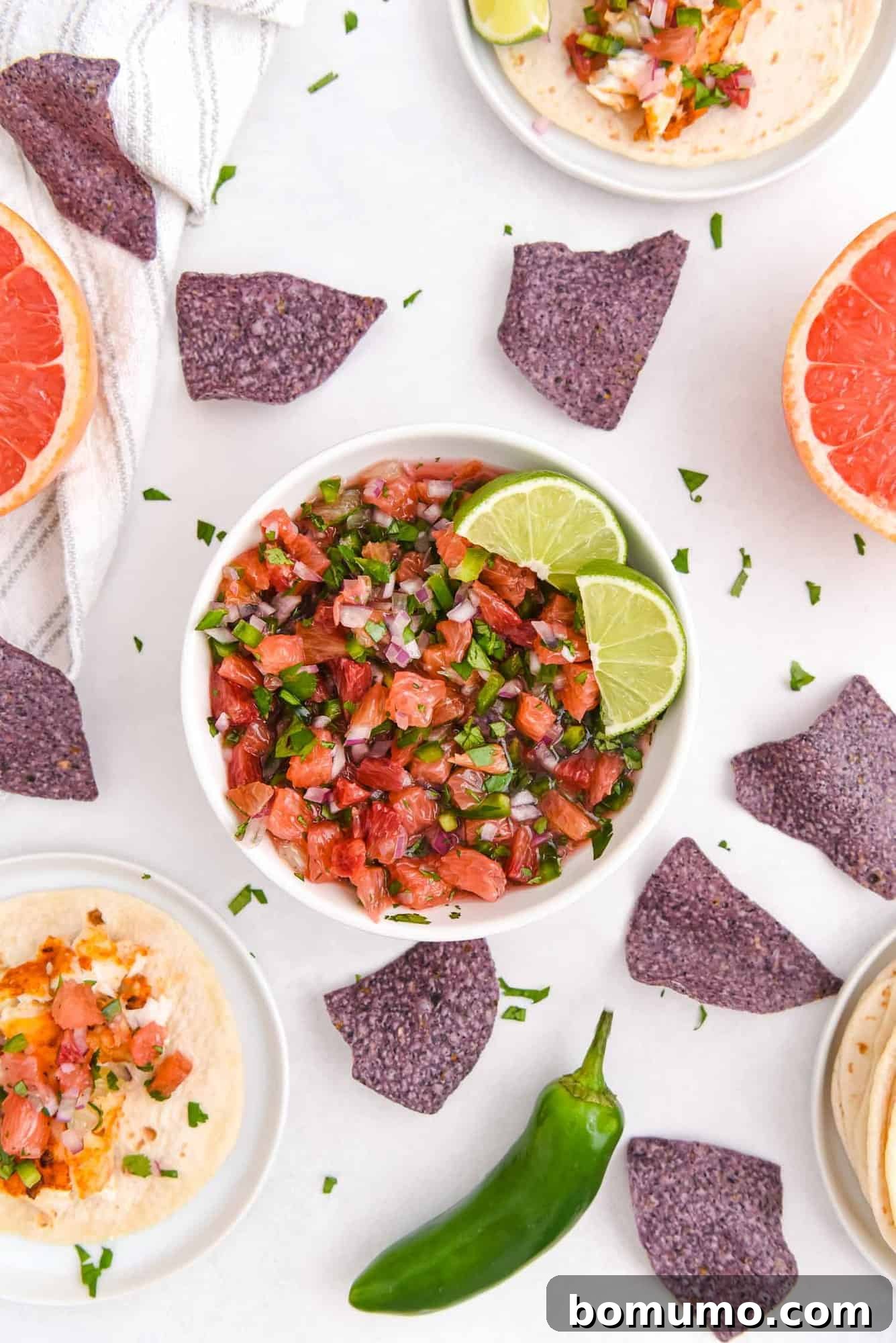 A beautifully arranged bowl of citrus salsa, surrounded by golden tortilla chips and the fresh, whole ingredients of grapefruit, oranges, and cilantro.