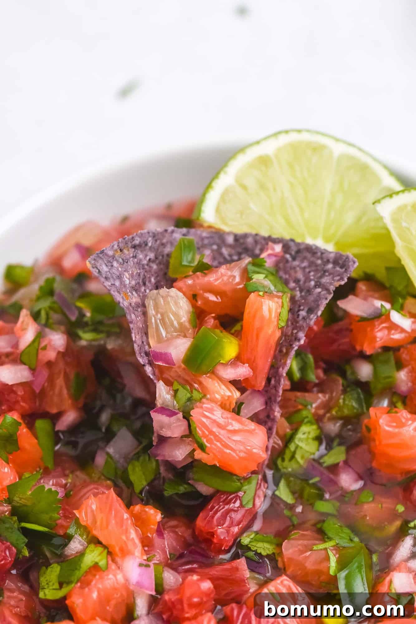 Close-up shot of a blue corn chip generously topped with vibrant citrus salsa, showcasing segments of grapefruit and oranges.