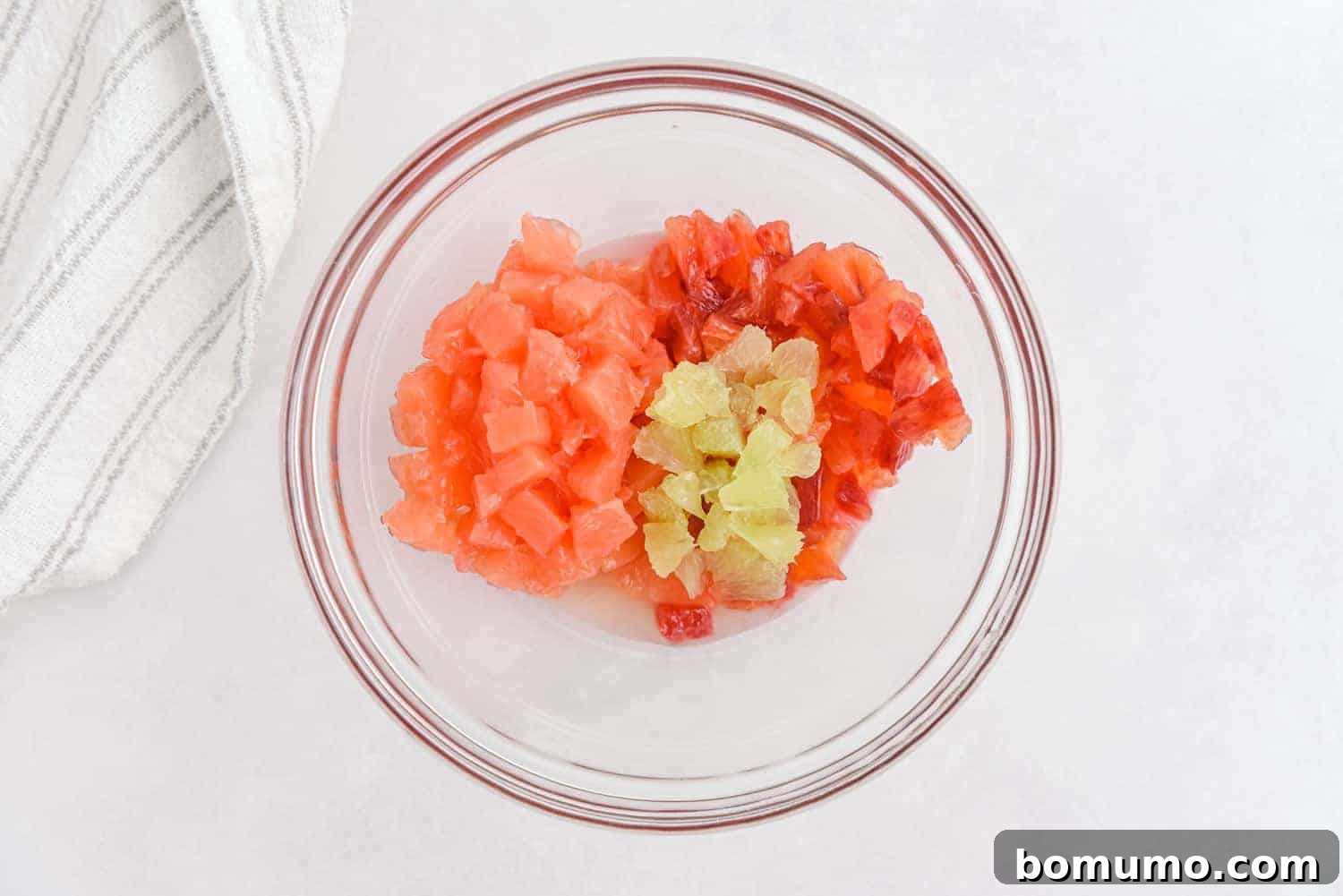 Close-up of freshly diced grapefruit, oranges, and lime segments in a clear bowl, ready to be combined into salsa.
