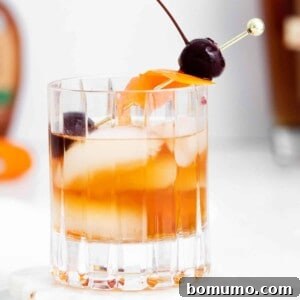 An old fashioned cocktail on ice with an orange peel and cherries.