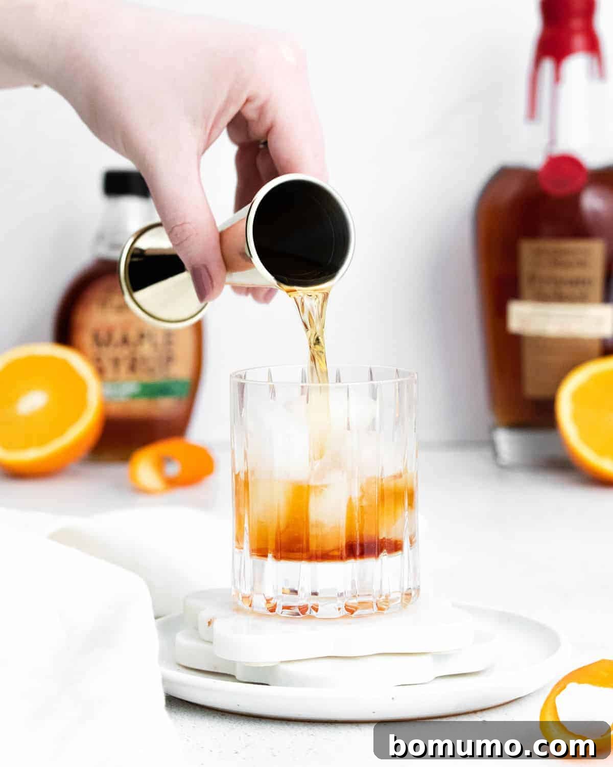Rich amber-colored bourbon being poured gracefully over a large ice cube in a classic old fashioned glass, highlighting the drink's appealing hue and refreshing chill.