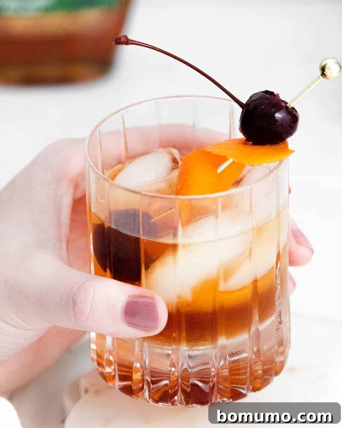 A close-up of a female's hand gracefully holding a classic old fashioned cocktail, showcasing its rich amber color and elegant presentation.