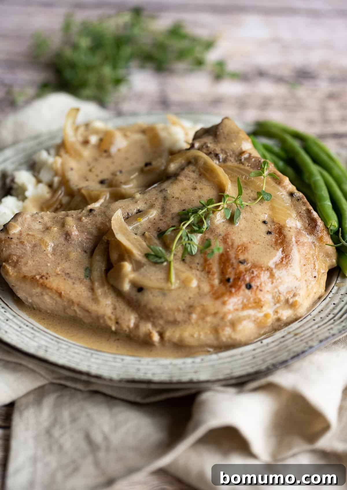 A perfectly cooked smothered pork chop on a plate, generously covered with creamy mushroom and onion gravy, served alongside fresh green beans.