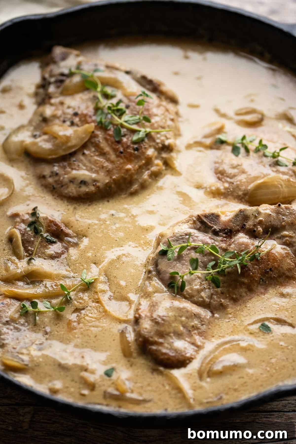 Two smothered pork chops served on a plate, generously covered in a creamy gravy, with a sprig of fresh thyme as garnish.
