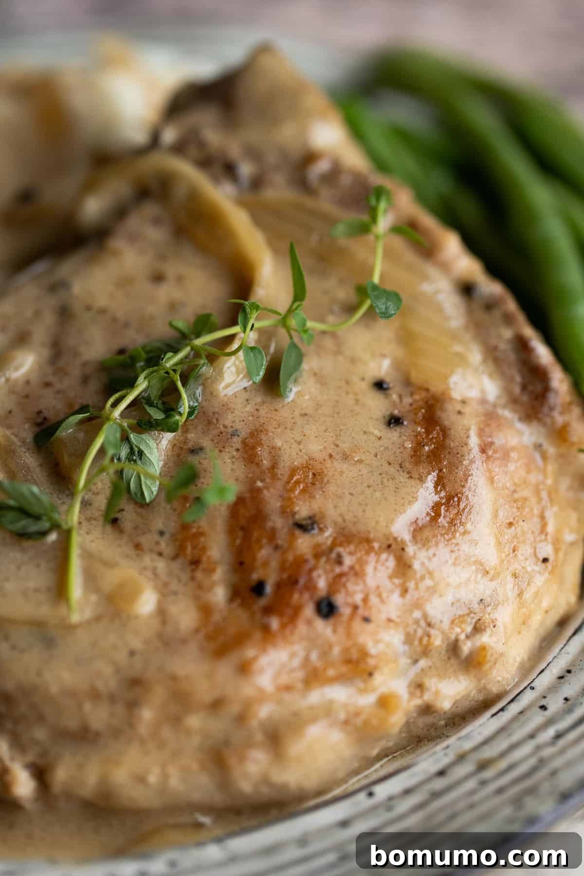 A close-up view of a perfectly cooked smothered pork chop, showing its tender interior and the rich, creamy gravy clinging to it.