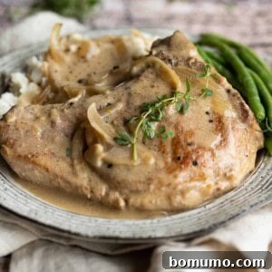 Close-up of a plate of smothered pork chops with gravy and thyme.