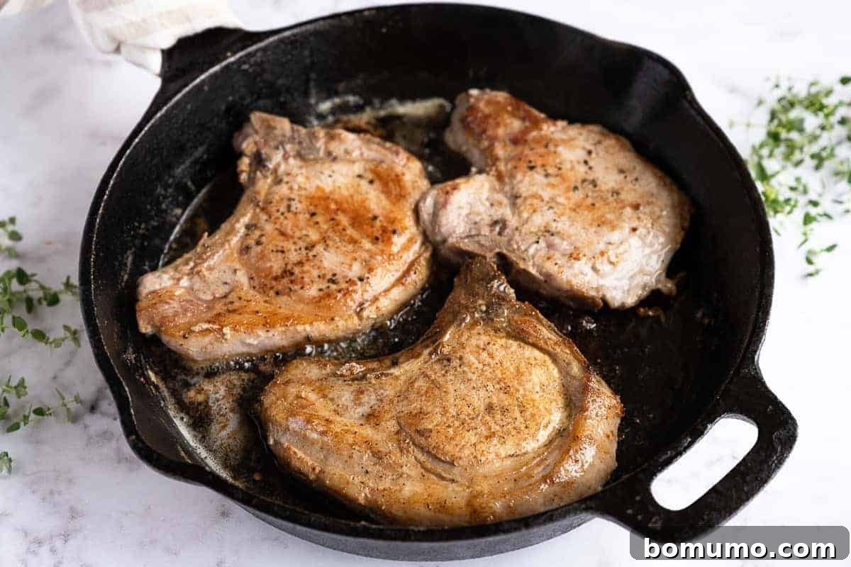 Two beautifully browned pork chops sizzling in a cast iron skillet, showcasing a perfect golden-brown crust.
