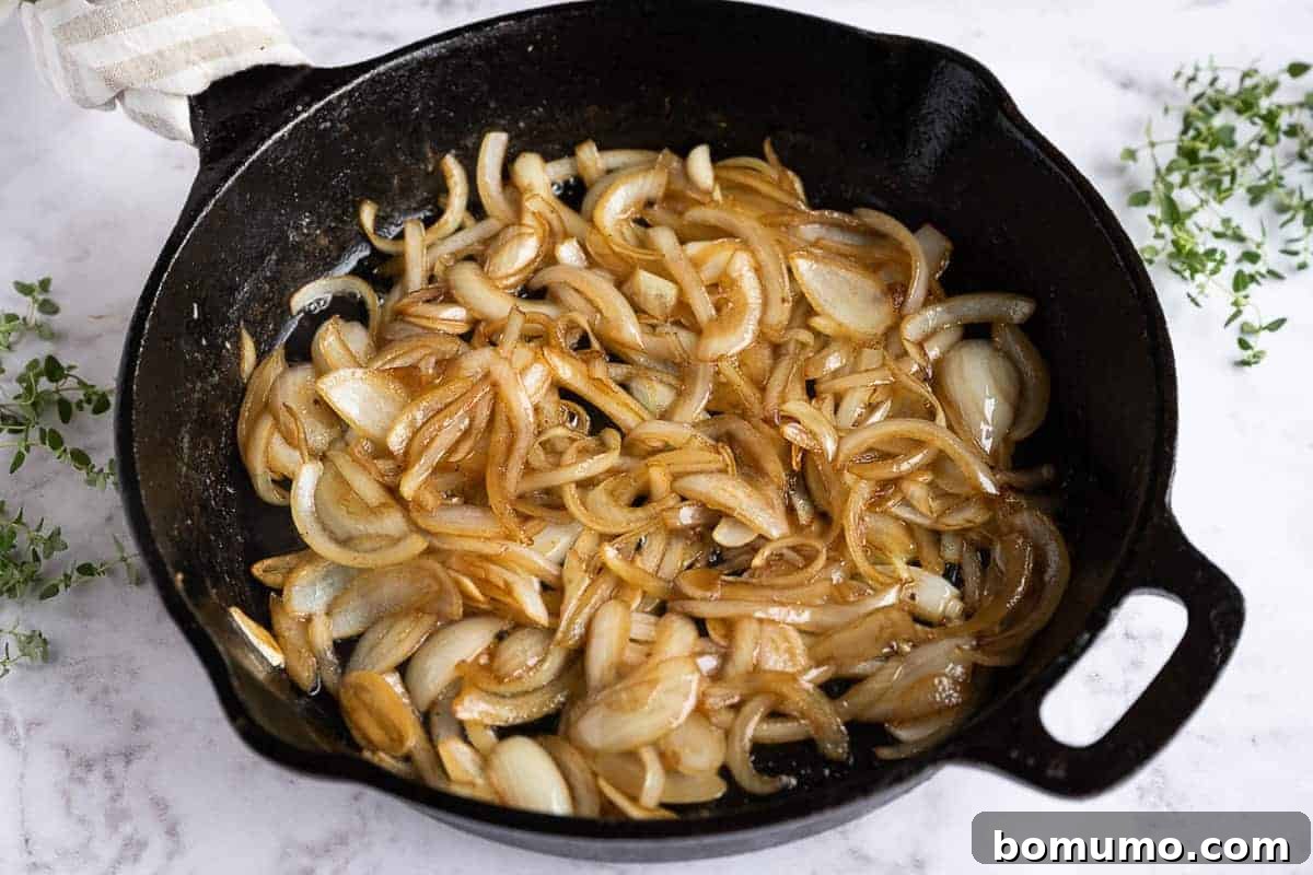 Sautéed onions, softened and translucent, glistening in a cast iron skillet, forming the flavor base for the sauce.