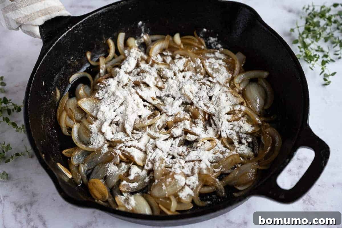 Flour being sprinkled and stirred over sautéed vegetables in a skillet, creating a thick, pasty roux.