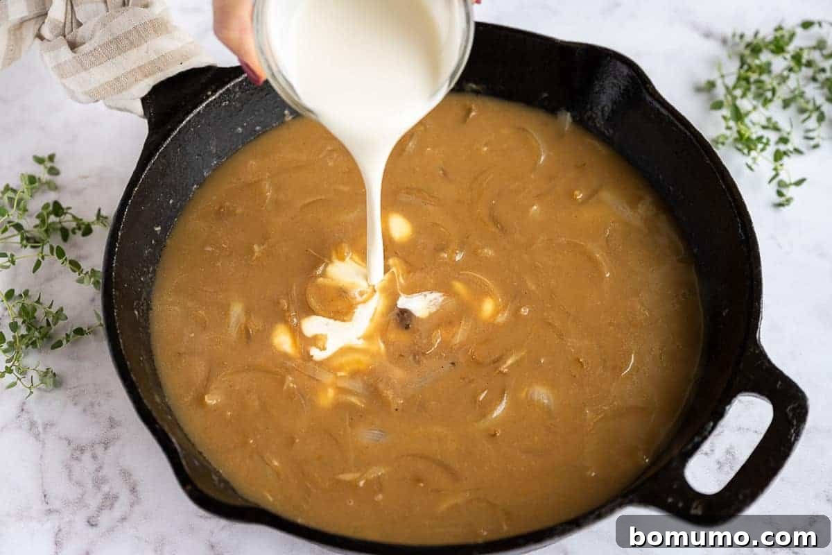 A stream of heavy cream being poured into the rich, brown gravy in a skillet, enhancing its creamy texture.