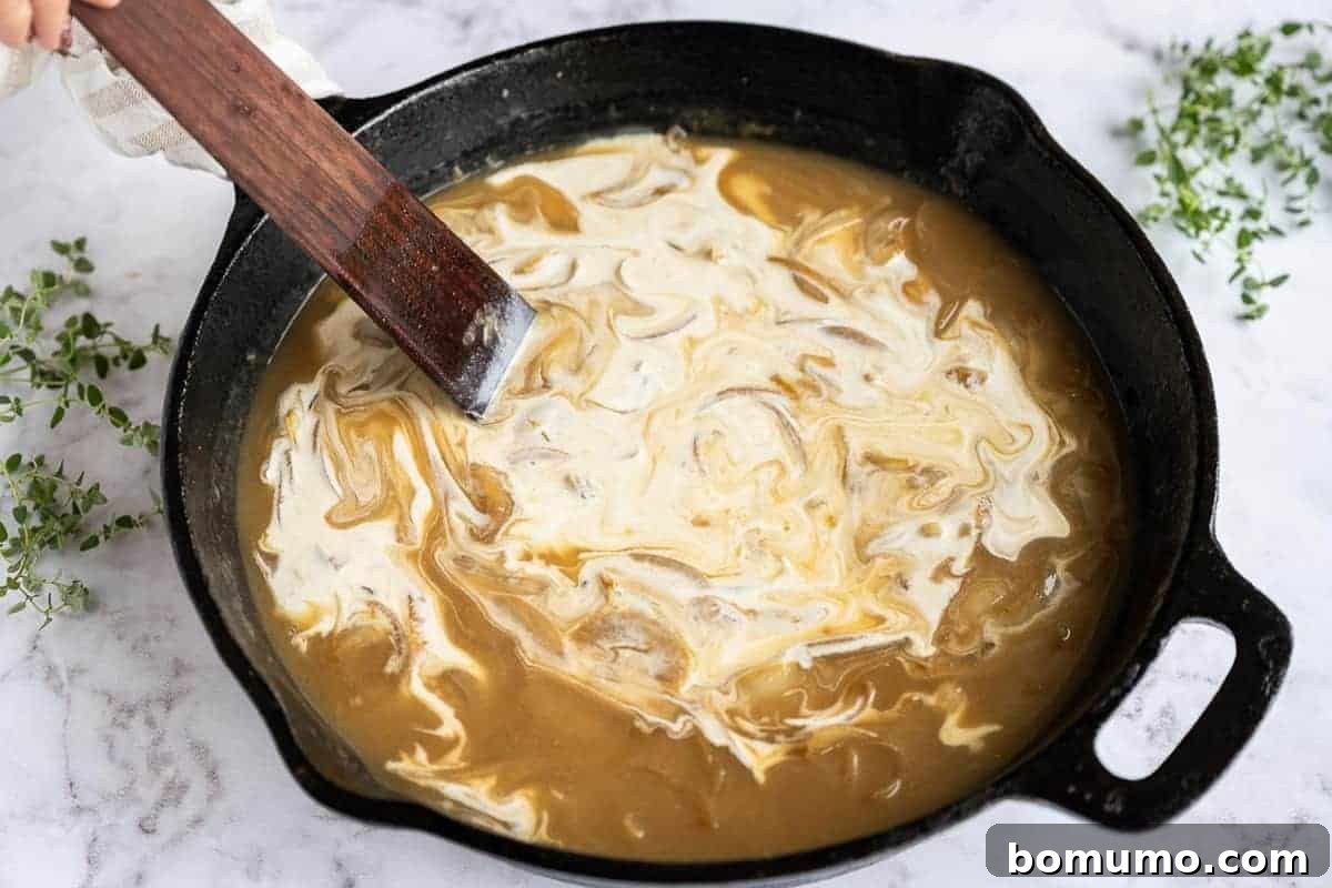 Heavy cream being carefully stirred into the developing sauce in a skillet, creating a smooth and rich consistency.