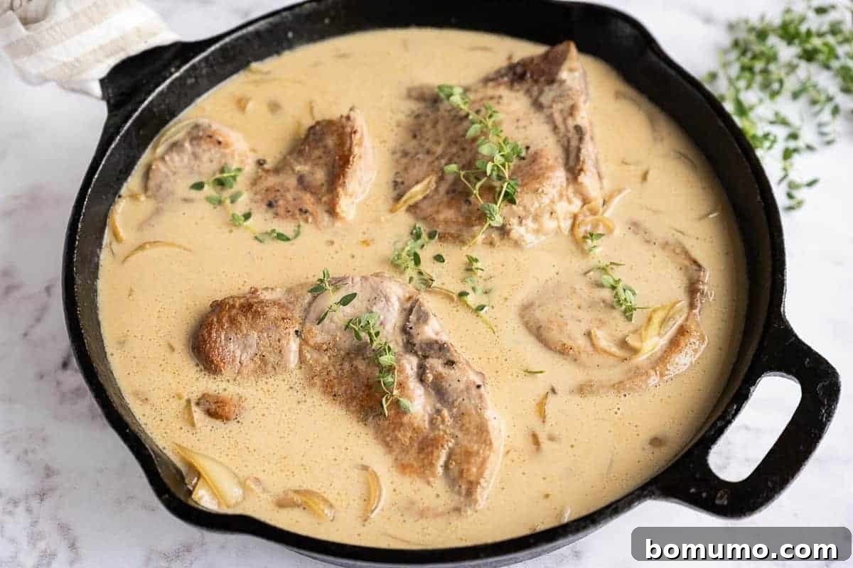Succulent pork chops simmering in a rich, creamy gravy, adorned with fresh thyme sprigs, under a covered skillet.