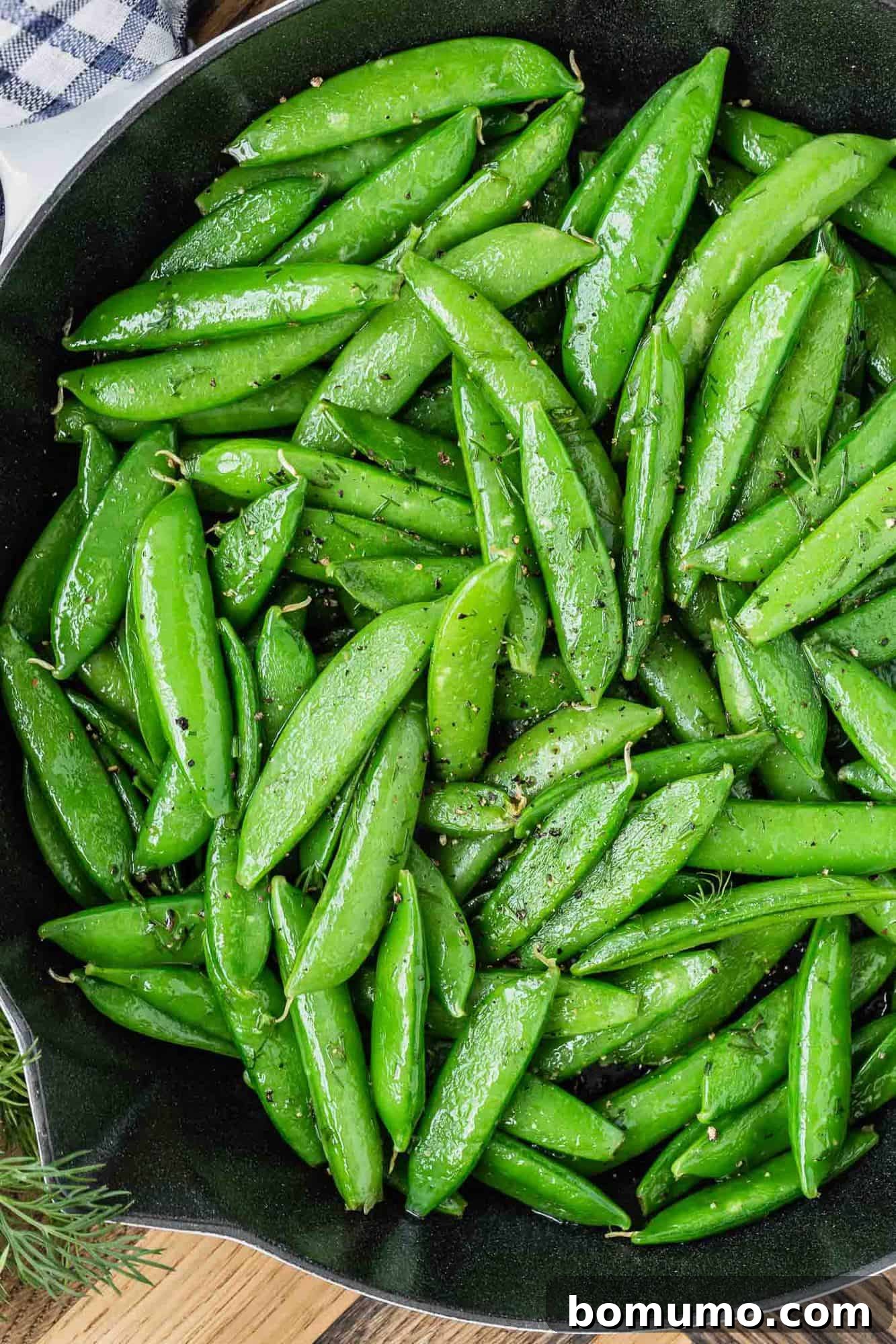 Close up of cooked snap peas in a black skillet.