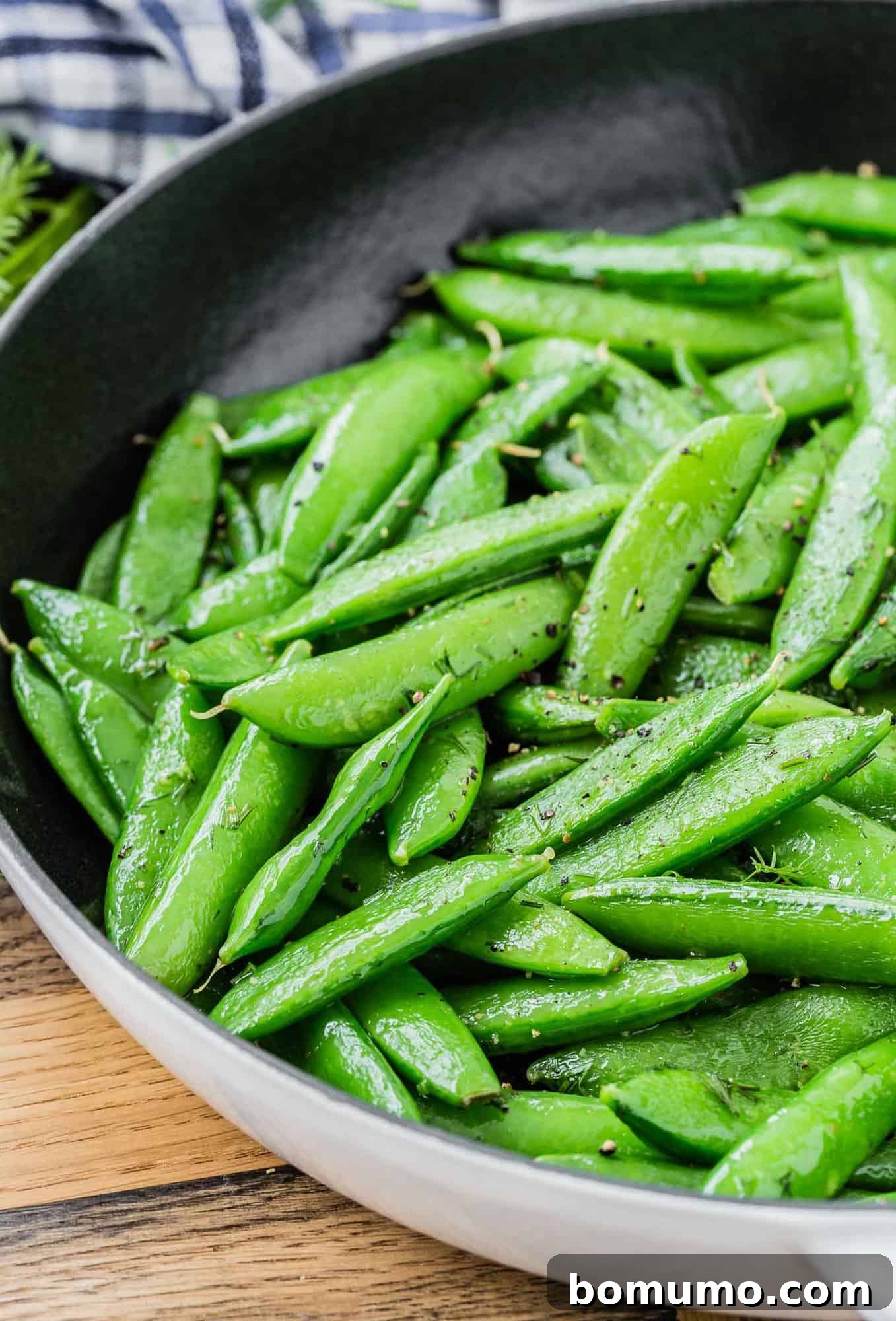 Sugar snap peas in a black and white skillet on a wooden surface.
