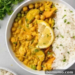 A hearty vegetarian curry in a white bowl, served with rice and garnished with a fresh lemon slice.