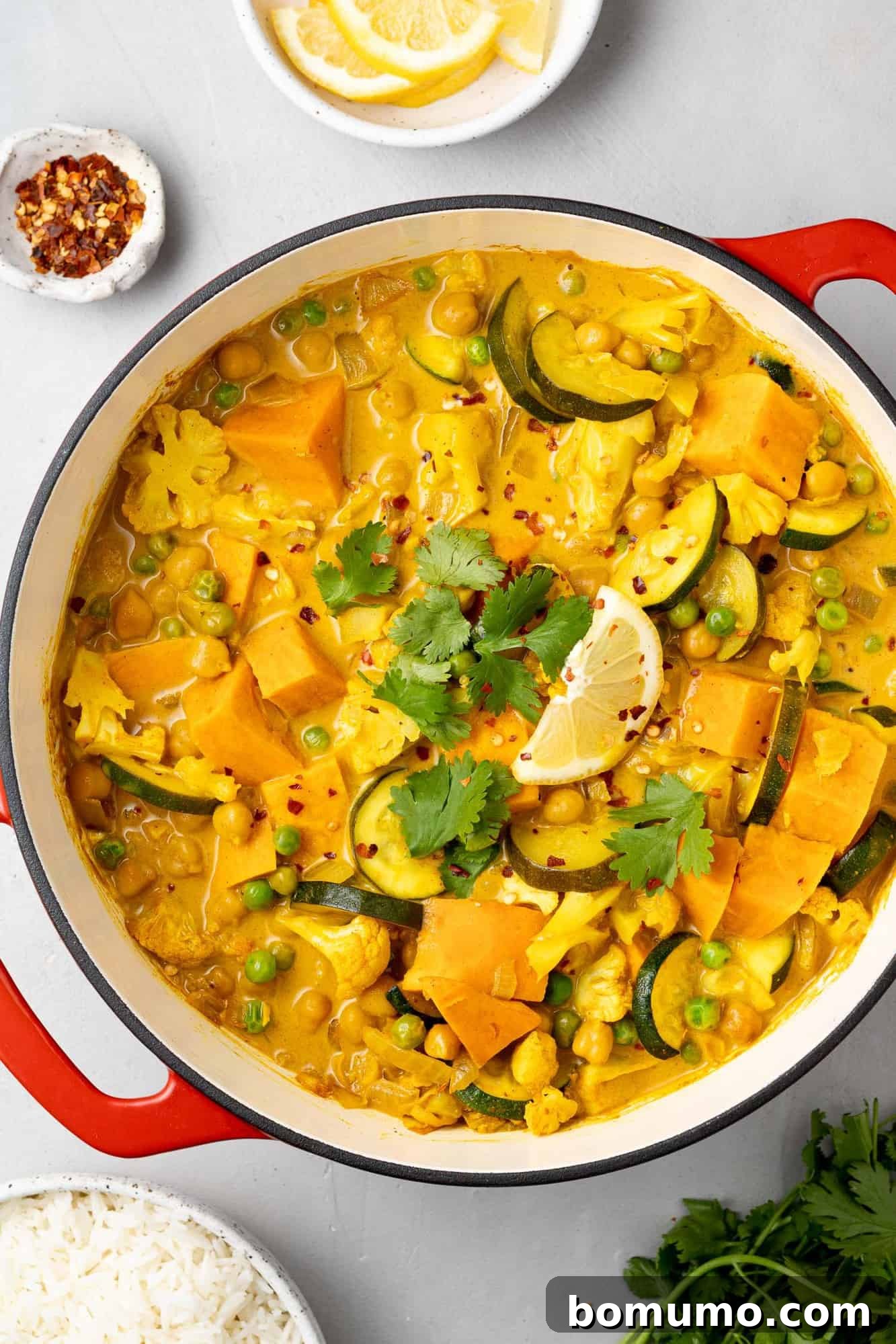 An inviting overhead view of a vegetarian curry simmering gently in a large Dutch oven, showcasing chunks of sweet potatoes, chickpeas, and cauliflower in a rich sauce.