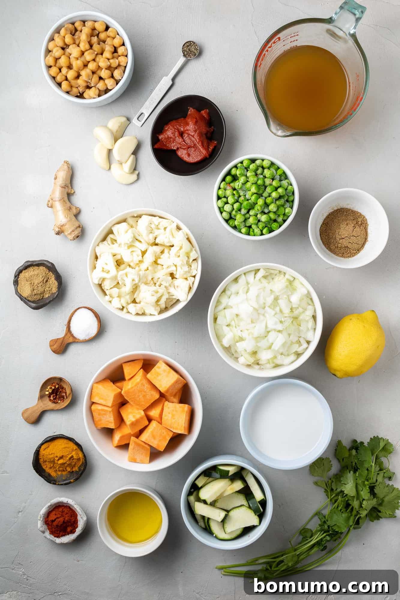 An overhead shot showcasing the fresh ingredients for vegetarian curry: vibrant spices, hearty chickpeas, florets of cauliflower, chunks of sweet potatoes, and bright green peas, ready for cooking.