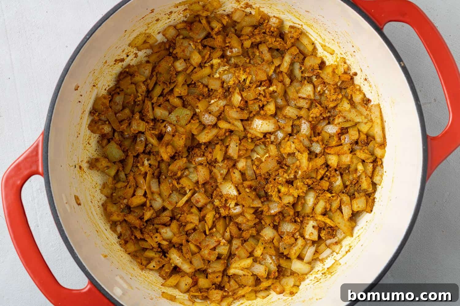 Freshly chopped vegetables, including cauliflower and sweet potatoes, gently sautéing in a large red Dutch oven, preparing the base for a rich curry.