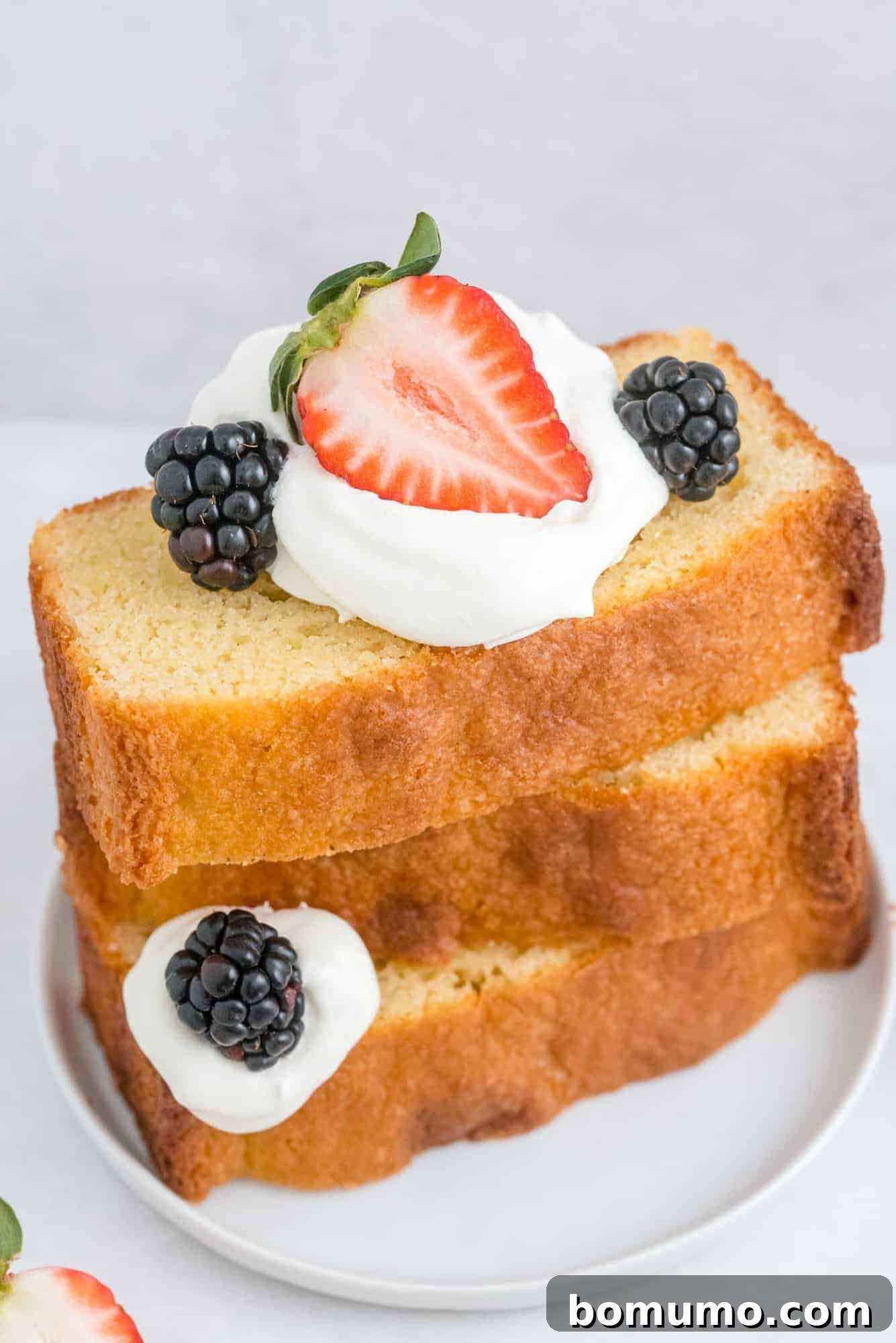 Timeless Pound Cake Perfection 2 Stacked slices of golden pound cake adorned with vibrant fresh fruits and berries, showcasing its rich texture and versatility as a dessert.