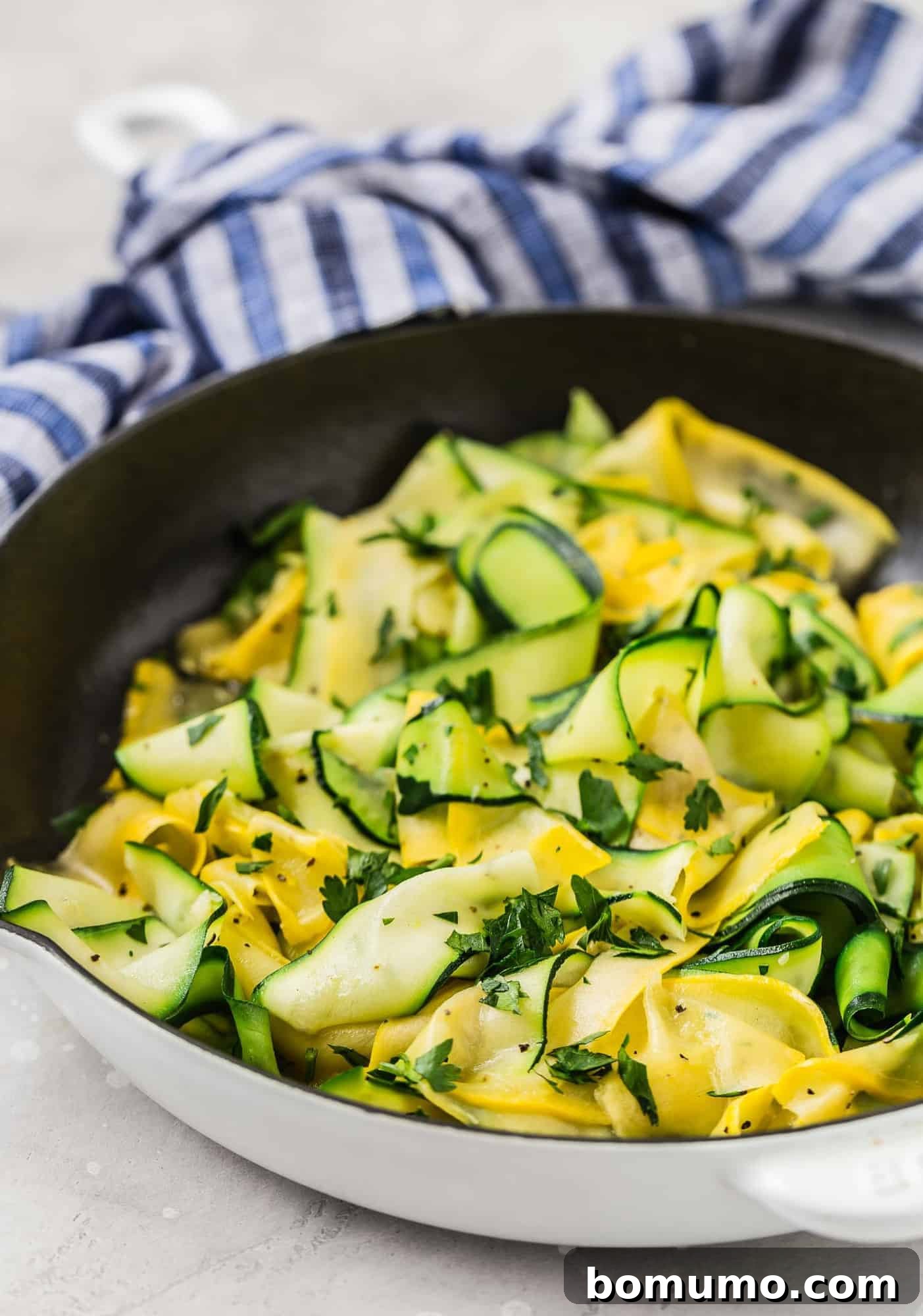 Artfully arranged summer squash and zucchini ribbons in a black and white skillet, set against a charming blue and white linen for a rustic touch.
