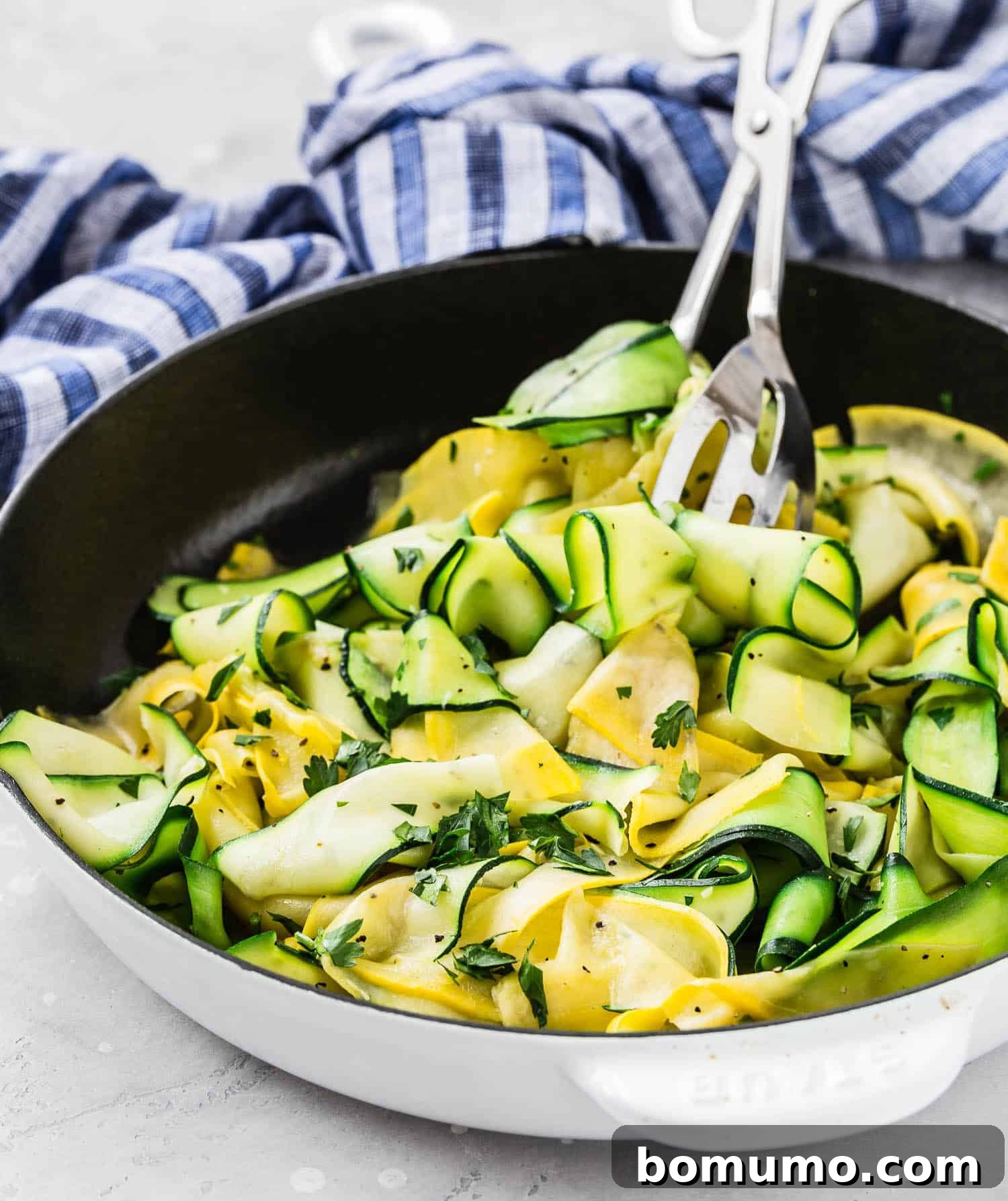 Delicate ribbons of zucchini and vibrant summer squash being expertly tossed with tongs in a frying pan, illustrating the cooking process.