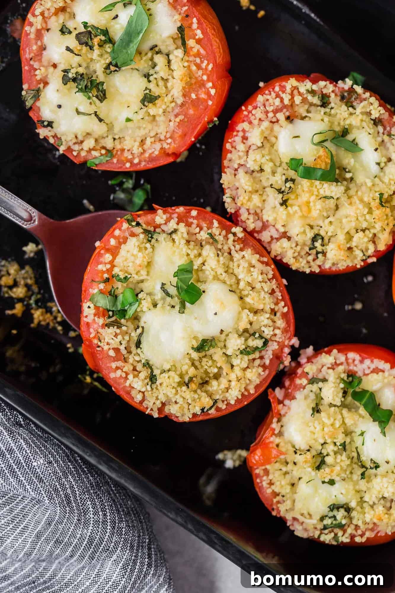 Overhead view of caprese stuffed tomatoes, one with a spatula under it.