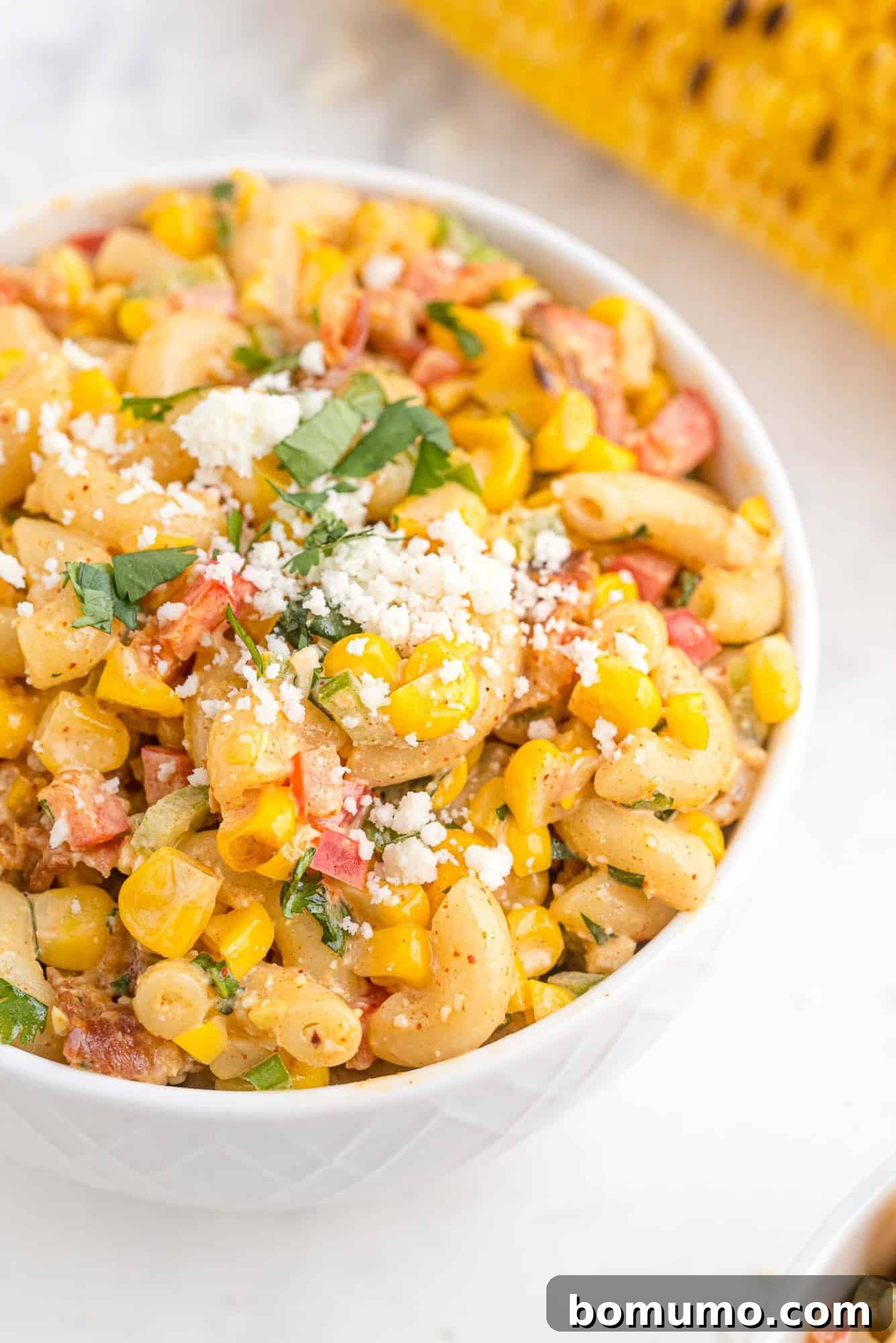 A vibrant Mexican street corn pasta salad, brimming with corn and cheese, served in a pristine round white bowl, ready to be enjoyed.